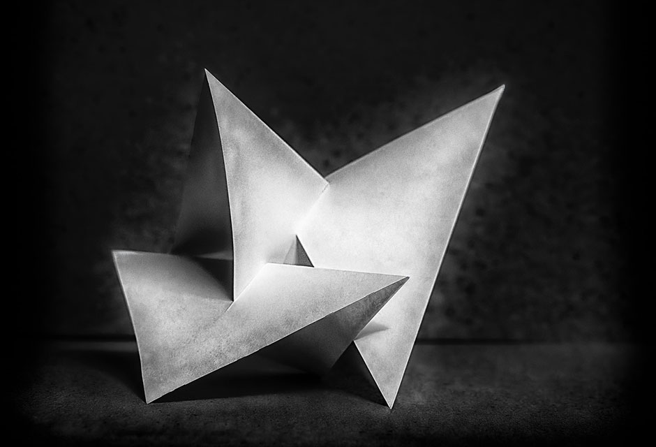 Schwarz-weiße Nahaufnahme von gefalteten dreieckigen Papierfiguren auf dunklem Untergrund