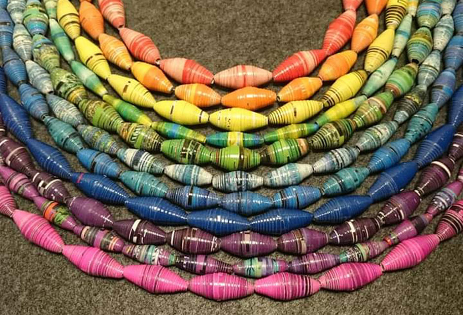 Bänder mit aufgefädelten Perlen in verschiedenen Farben liegen als Halbkreis auf dem Boden und stellen einen Regenbogen dar.