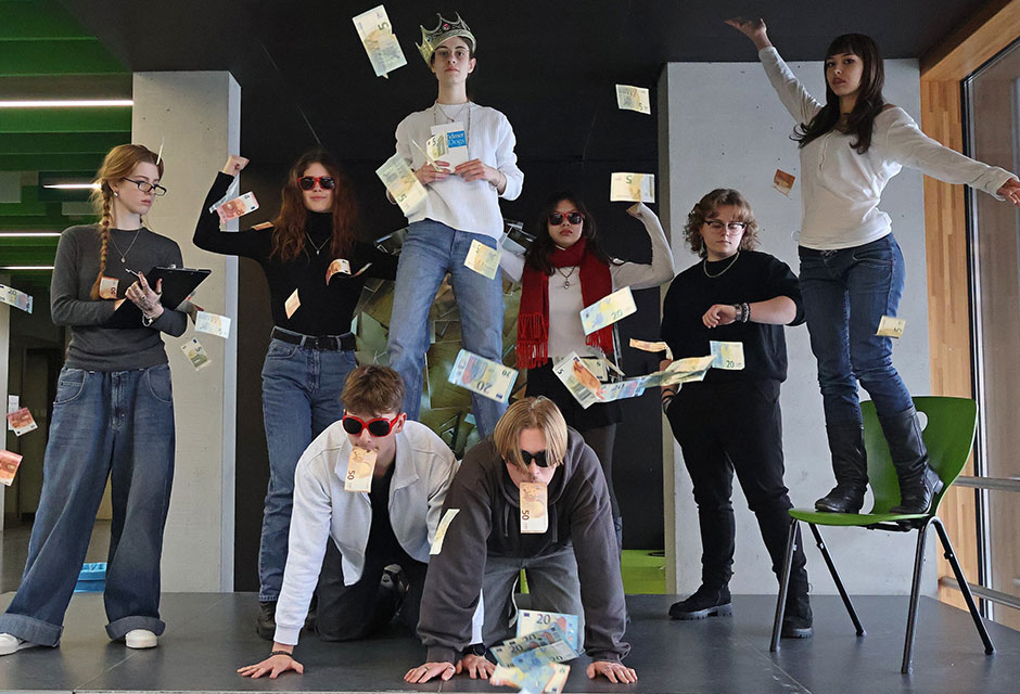 Gruppe von Menschen in verschiedenen Posen, umgeben von durch die Luft fliegenden Geldscheinen. Eine Person mit Krone steht auf den Rücken zweier knienden Menschen mit Geldscheinen im Mund