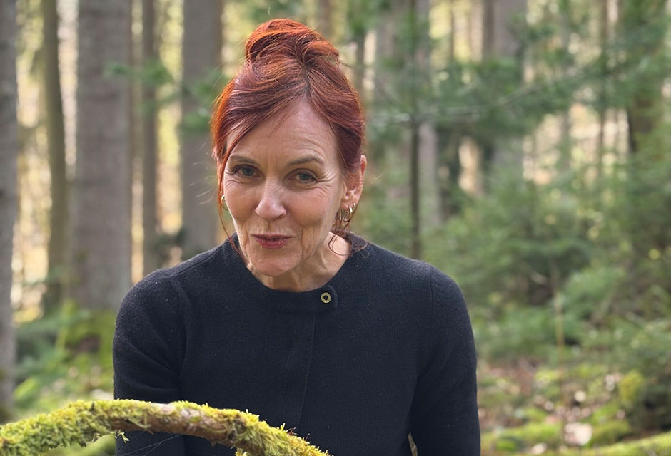 Frau mit orangefarbenen Haaren, die zum Zopf zusammengebunden sind und dunkelblauem Pullover ist im Wald.