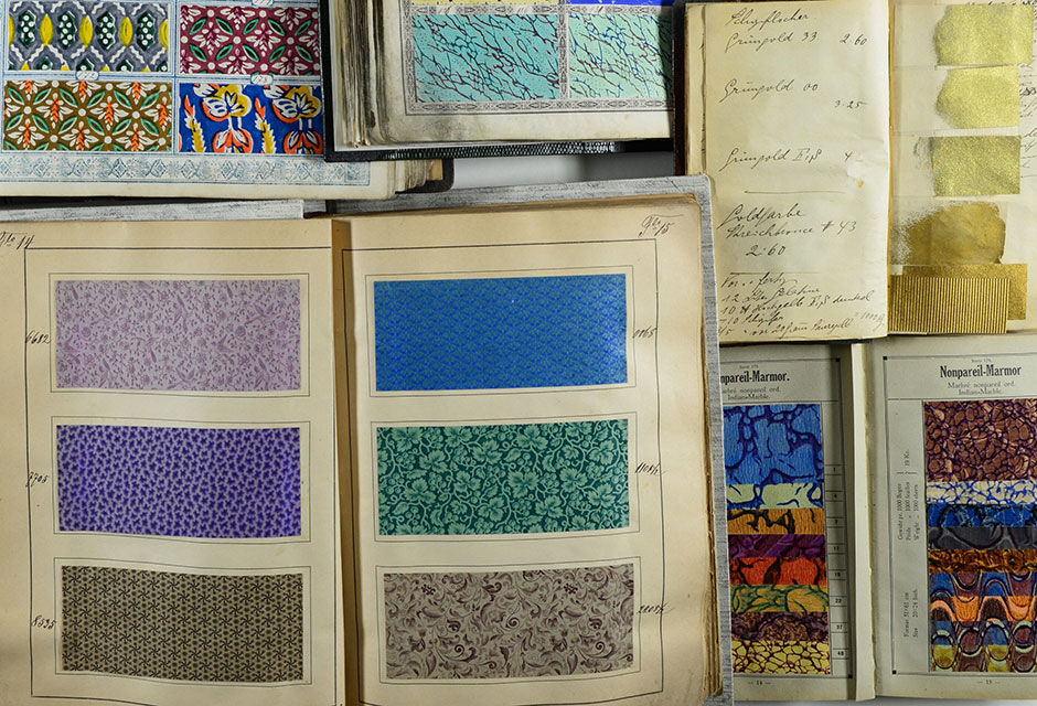 Mehrere aufgeschlagene Musterbücher mit farbigen Papier- und Stoffmustern und einem Buch mit handschriftlichen Notizen