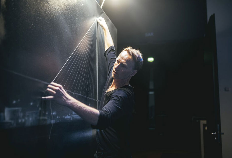 Person zeichnet gerade weiße Linien auf eine schwarze, hell angeleuchtete Leinwand