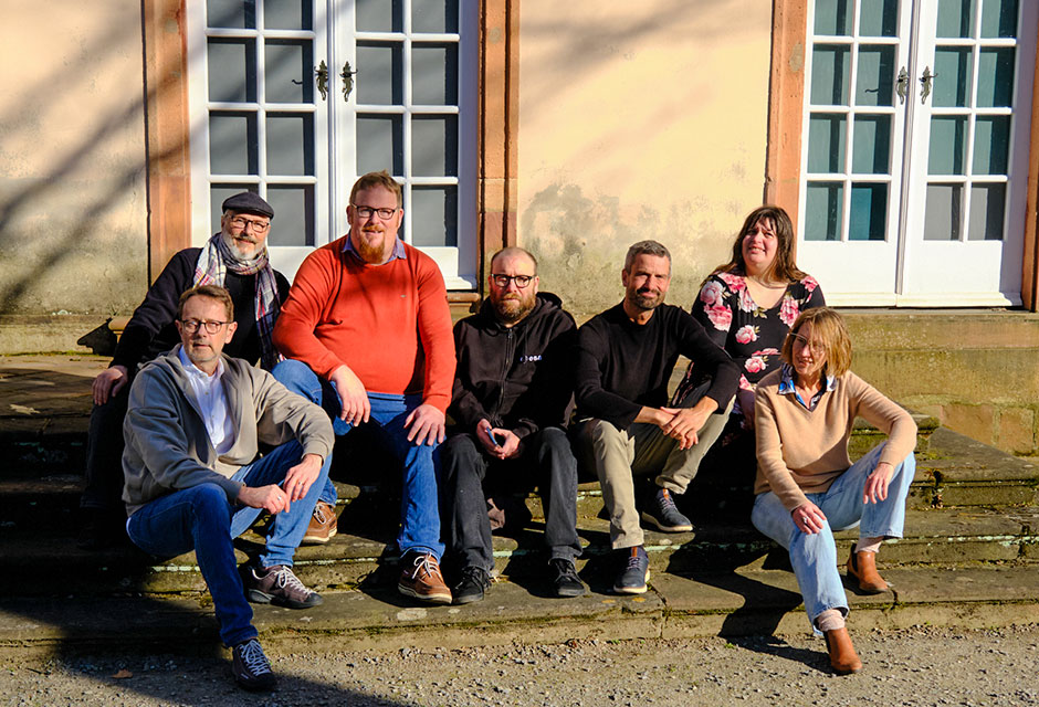 Gruppe von sieben Menschen sitzt auf einer Steintreppe vor einem Gebäude.