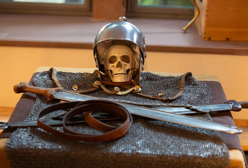 Kettenhemd mit Helm, Schwertern, Ledergürtel und einem Schädel auf Holztisch arrangiert