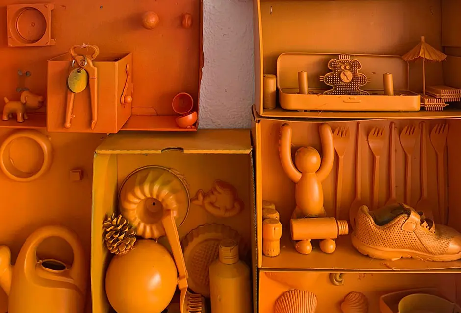 Kartons mit vielen Gegenständen darin hängen an einer Wand. Alles ist orange gefärbt.