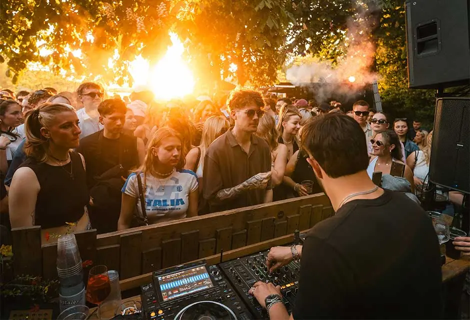 Viele junge Menschen im Sonnenuntergang vor einem DJ-Pult mit DJ